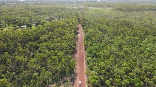 High Slow moving Aerial Drone shot of Following Car Driving on Long Straight Red Road and Green Bush