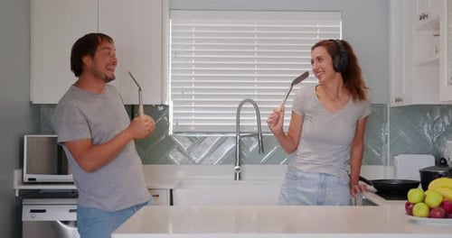 Couple Singing with Cooking Utensils in Kitchen
