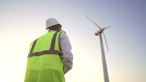 Engineer in a Yellow Vest and a White Helmet Suitable To the Windmill To Check Its Working Condition