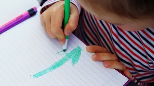 Child Drawing Arrow with Green Marker in Notebook