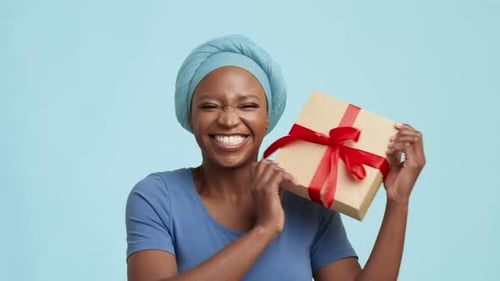 Cheerful African American Woman Shaking Present Box On Blue Background