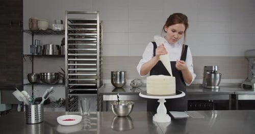Woman Decorating Cake with Frosting in Commercial Kitchen