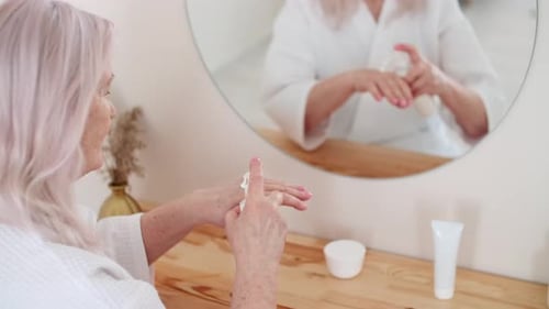 Senior Woman Applies Cream to Hands in Bathroom