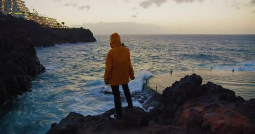 A Young Girl Watching the Ocean at the Edge on Top of a Rocky Seashore in