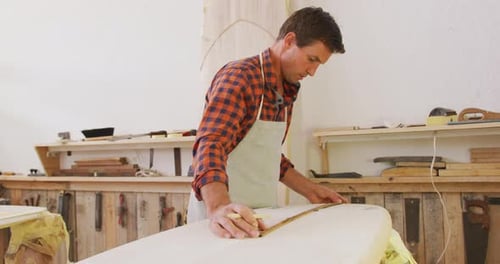 Caucasian male surfboard maker checking a surfboard after polishing