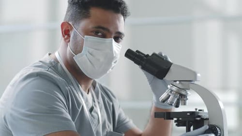 Portrait of Male Doctor in Mask Using Microscope