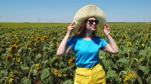 Adorable joven con sombrero de paja, falda amarilla y camiseta azul sonriendo en el campo de girasoles