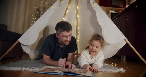 Father Reads Bedtime Story with Daughter in Tent
