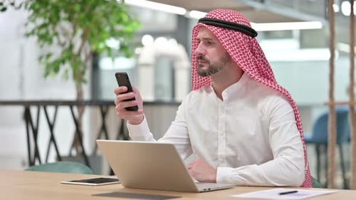 Man in Head Covering Using Smartphone at Desk