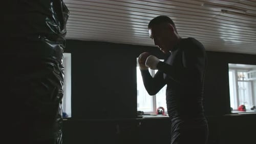 Man Punches Heavy Bag in Dark Boxing Gym