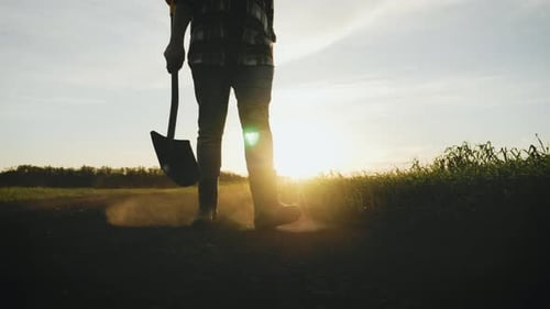 Farmer Walking with Shovel in Field at Sunset