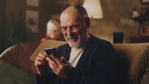 Senior Man Uses Smartphone on Couch at Home