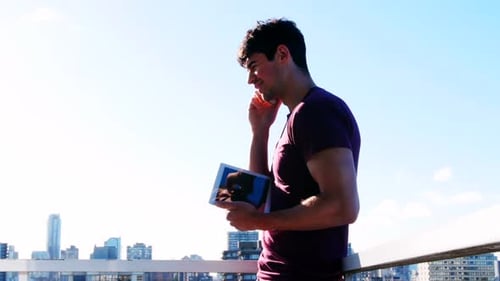 Young Man Using Tablet, Phone on City Rooftop