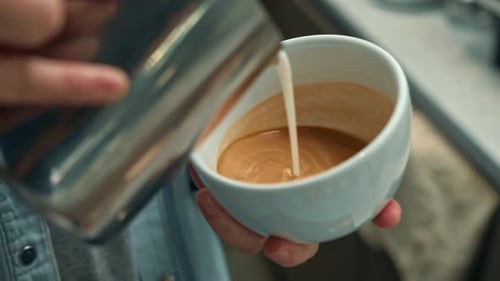 Barista making latte art in coffee shop. Professional man making pouring stream milk with espresso