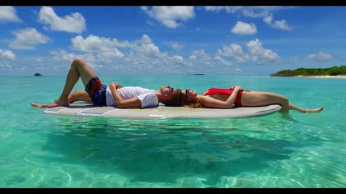 Two people sunbathe on relaxing shore beach adventure by turquoise lagoon and white sandy background
