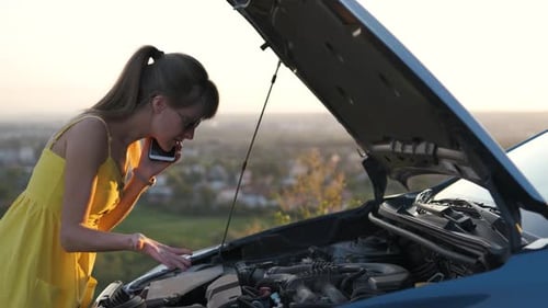 Young Woman Driver Talking on Mobile Phone Standing Near Her Car with Open Hood Having Motor Problem