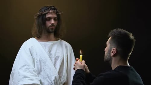 Man Kneeling Before Man in White Robe Holding Candle