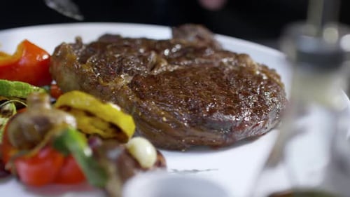 Steak Being Placed on Plate with Grilled Vegetables