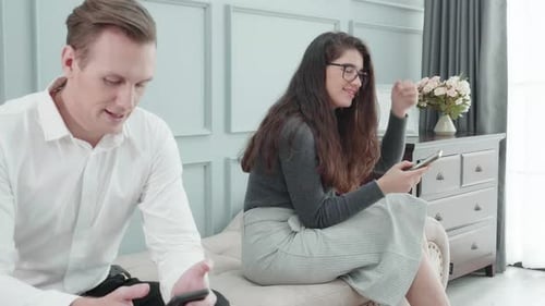 Young Couple Using Cellphones Sitting on Bench