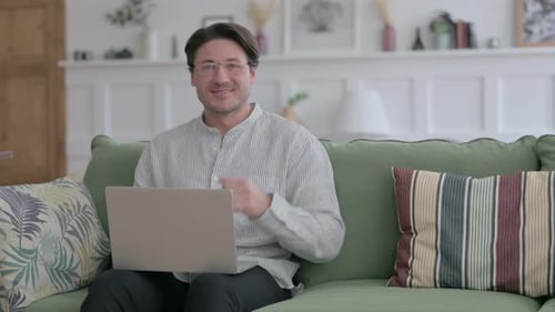 Man Using Laptop Gives Thumbs Up on Sofa