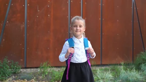 Smiling Girl with Backpack in Front of Wall