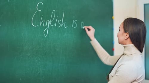 Young pedagogue writes on a blackboard with a chalk in the educational center.