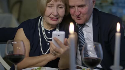 Happy Senior Couple Using Smartphone at Restaurant