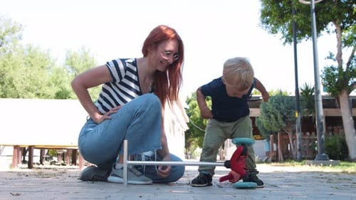 Child Plays with Scooter as Mother Watches in Park
