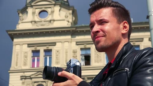 A Young Handsome Man Takes Photos with a Camera - Face Closeup From Below - a Quaint Yellow Building