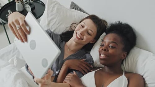 Multi-Ethnic Lesbian Couple with Tablet Relaxing in Bed