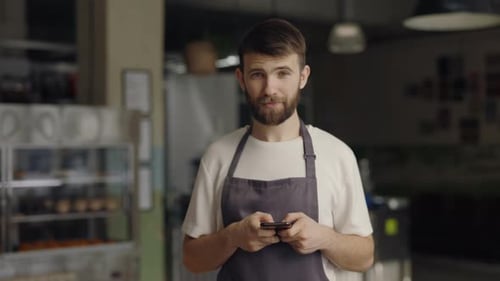 Caucasian Waiter in Apron Using Smartphone at Cafe