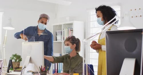 Office colleagues wearing face masks discussing over computer at office