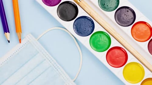 Schulmaterial mit Notizblock liegt auf einem pastellblauen Hintergrund mit einer medizinischen Maske