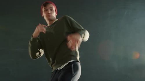 Portrait of Creative Male Dancer Dancing Indoors in Dark Hall with Lights in Background