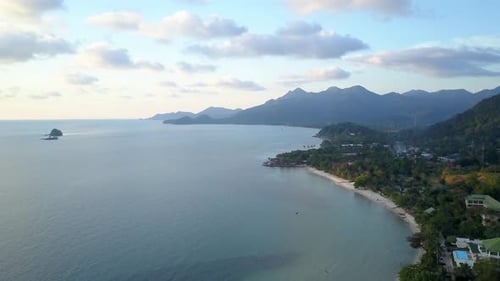 An aerial shot during a sunset from a drone over an island coast line, in the distance there are vis