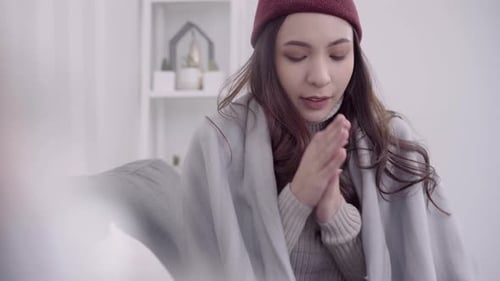 la femme ressent des maux de tête enveloppée dans une couverture grise, se mouche le nez et utilise un mouchoir en papier lorsqu'elle est allongée sur le canapé.