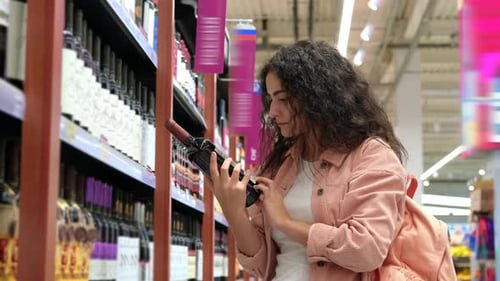 Woman Examining Wine Bottle in Supermarket Aisle