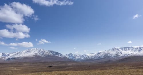 Timelapse of Sun Movement on Crystal Clear Sky with Clouds Over Snow Mountain Top. Yellow Grass at