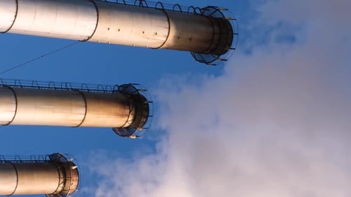 Industrial Chimneys Emitting Smoke Against Blue Sky