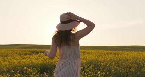 A Smiling Girl Is Running Across the Field and Holding on Her Hat