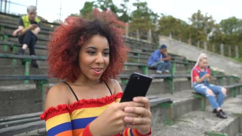Teen Girl Looks at Smartphone in Stadium Bleachers