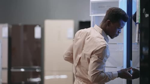 Young Afroamerican Guy is Choosing New Refrigerator in Home Appliance Store Buying Equipment for