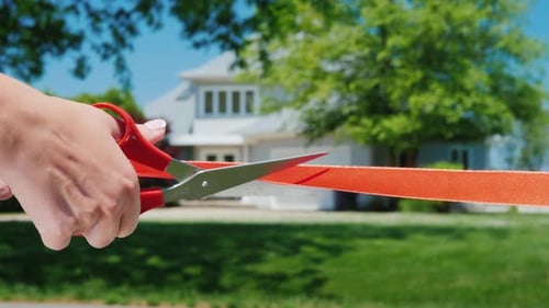 A Scissor-cut Arm Cuts a Red Ribbon, and a Typical American House Is Visible in the Background