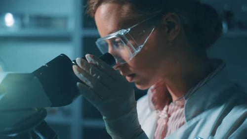 Woman Scientist Using Microscope in Dark Lab