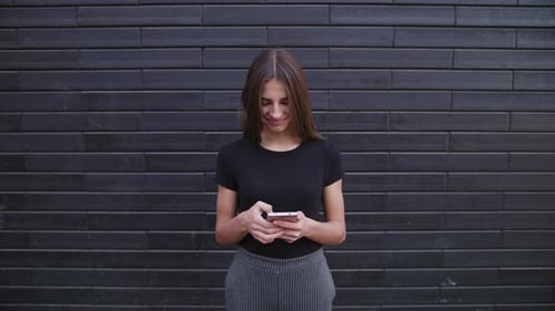 An Attractive Young Lady Wearing Glasses Using a Phone Against a Brick Wall Background. Close-up