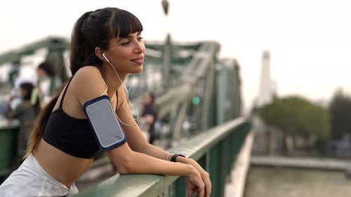 4K Hispanic woman listening to music from earphones while jogging in the city