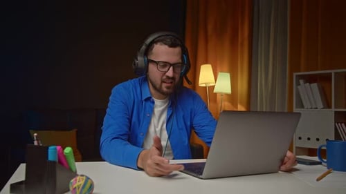 Man Talking on Laptop at Desk at Night