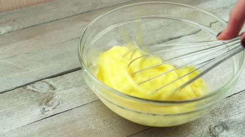 Footage of woman beating eggs in kitchen over wooden table