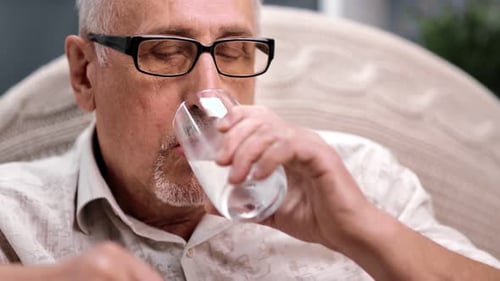 Senior Man Taking Pill with Water Indoors
