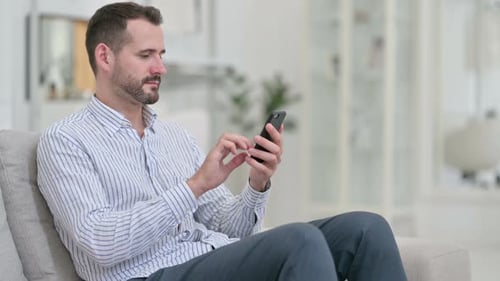 Man Using Smartphone Sitting on a Couch Indoors